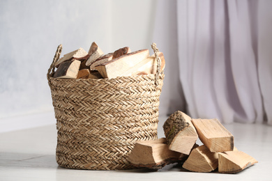 Wicker basket with cut firewood on white floor indoors