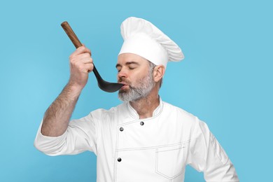 Photo of Chef in uniform tasting something on light blue background