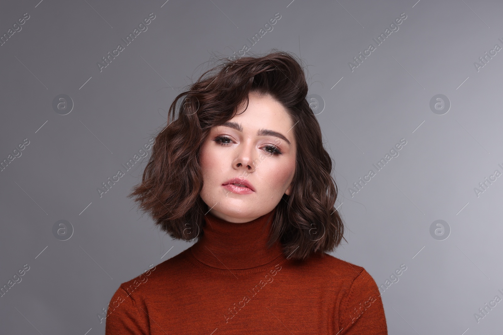 Photo of Portrait of beautiful young woman with wavy hairstyle on grey background