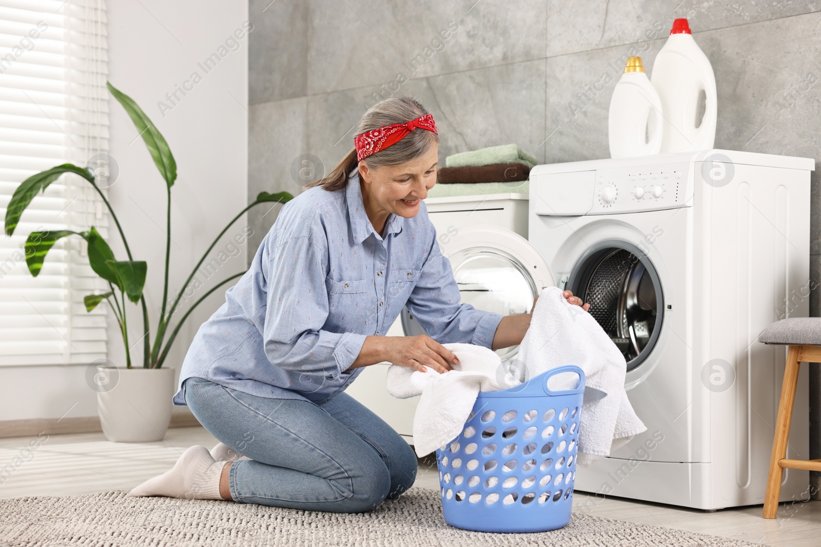 Photo of Happy housewife with laundry basket near washing machine at home