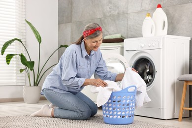 Happy housewife with laundry basket near washing machine at home