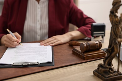 Notary signing document at wooden table in office, closeup