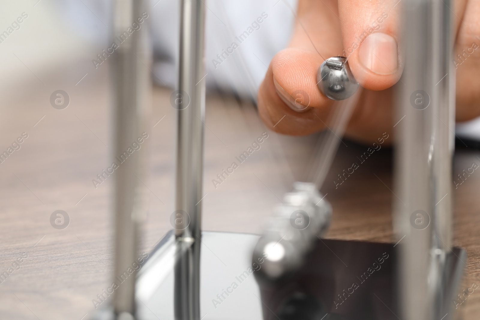 Photo of Man playing with Newton's cradle at table, closeup. Physics law of energy conservation