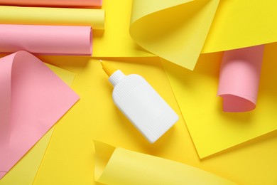Bottle of glue and colorful paper on yellow background, flat lay