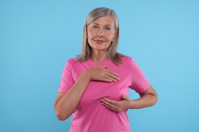 Photo of Beautiful senior woman doing breast self-examination on light blue background