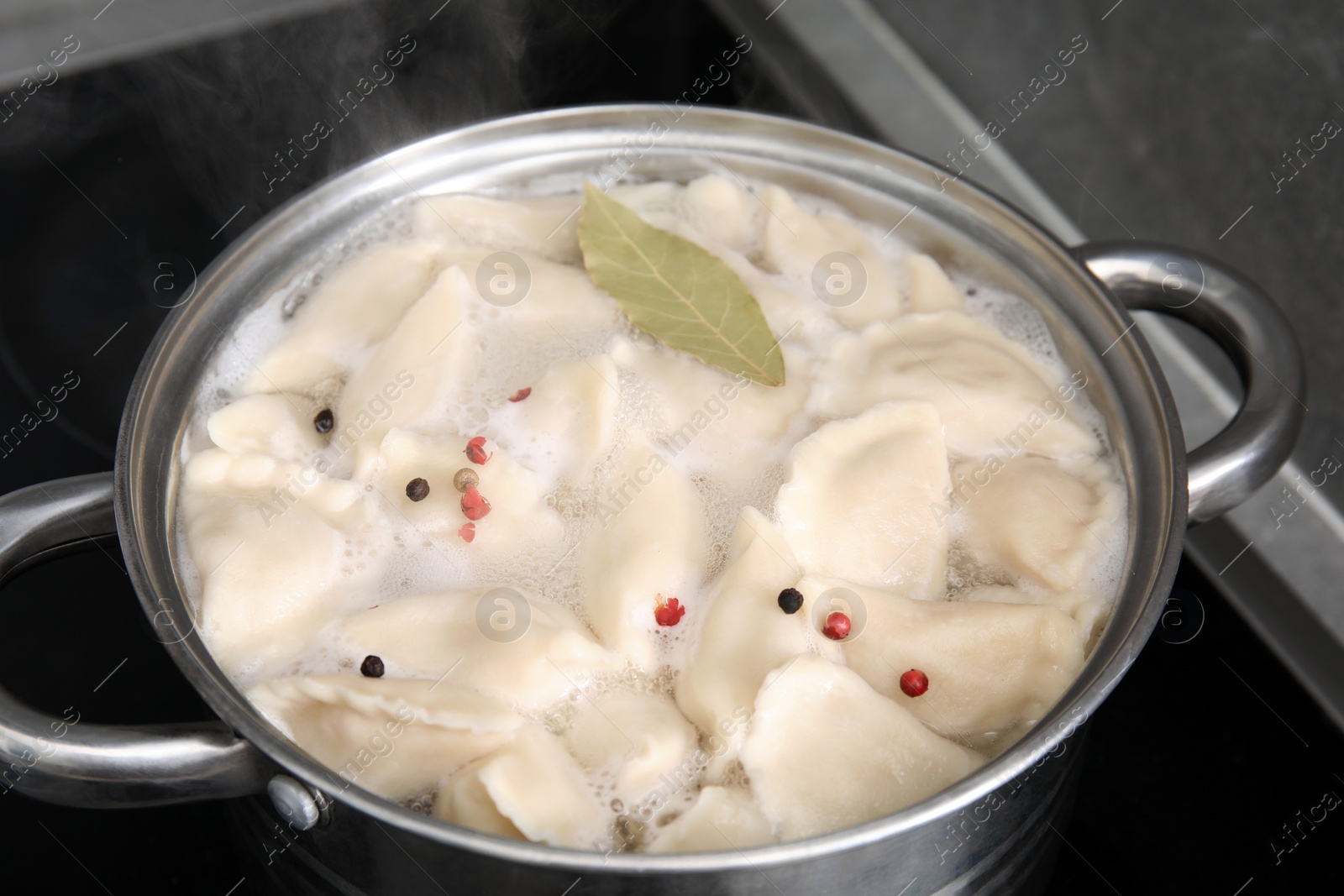 Photo of Cooking dumplings (varenyky) with tasty filling, peppercorns and bay leaf in pot indoors, closeup