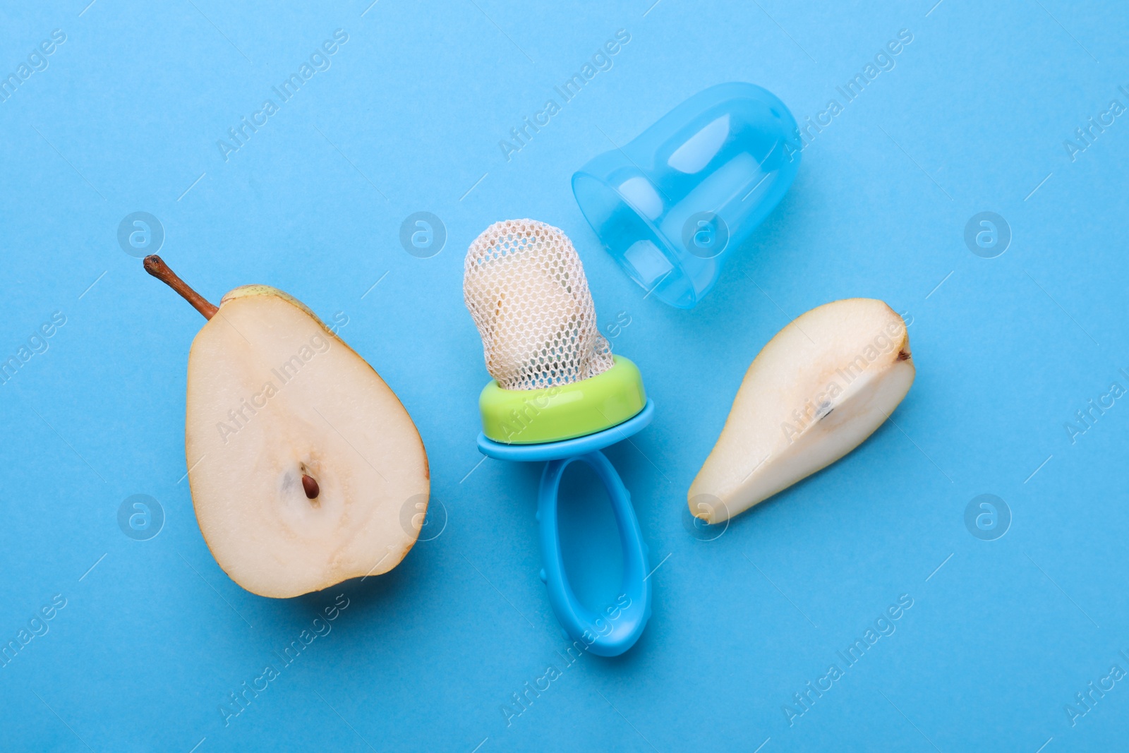 Photo of Nibbler with fresh pear on light blue background, flat lay. Baby feeder
