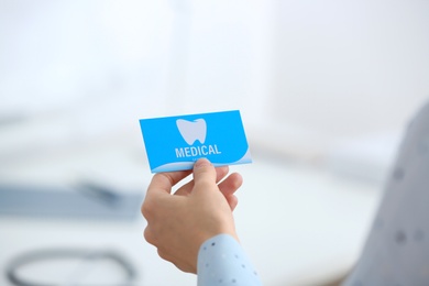 Photo of Woman holding business card indoors, closeup. Dental medical service
