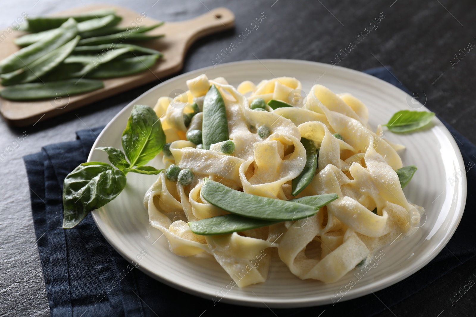 Photo of Delicious pasta with green peas and creamy sauce on black table