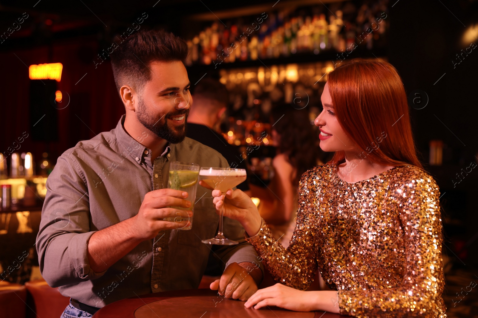 Photo of Happy couple clinking glasses with fresh cocktails at table in bar