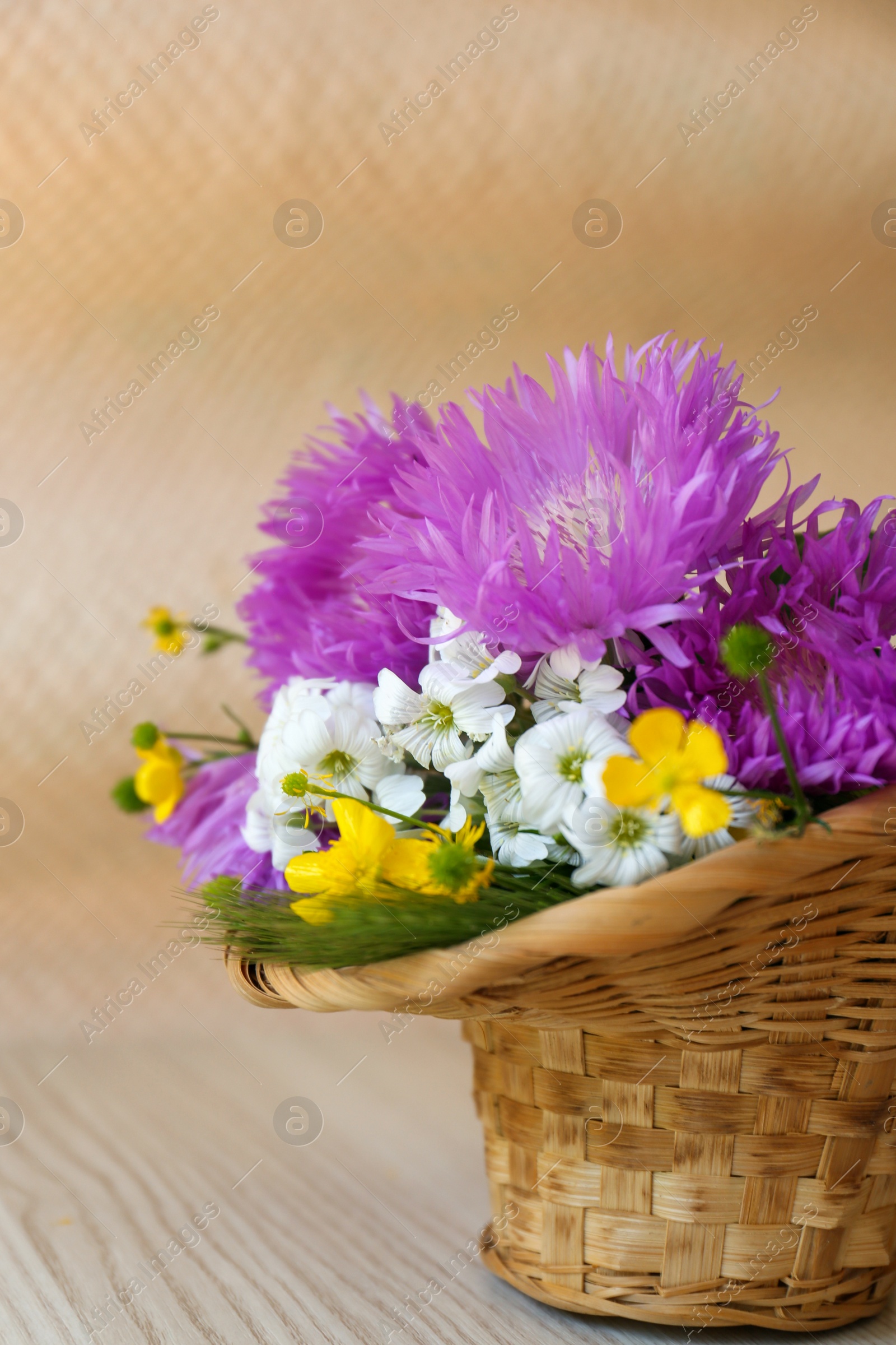 Photo of Bouquet of beautiful wildflowers in wicker basket on wooden table, closeup