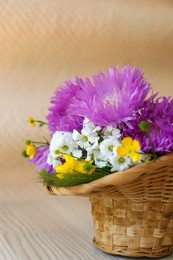 Photo of Bouquet of beautiful wildflowers in wicker basket on wooden table, closeup