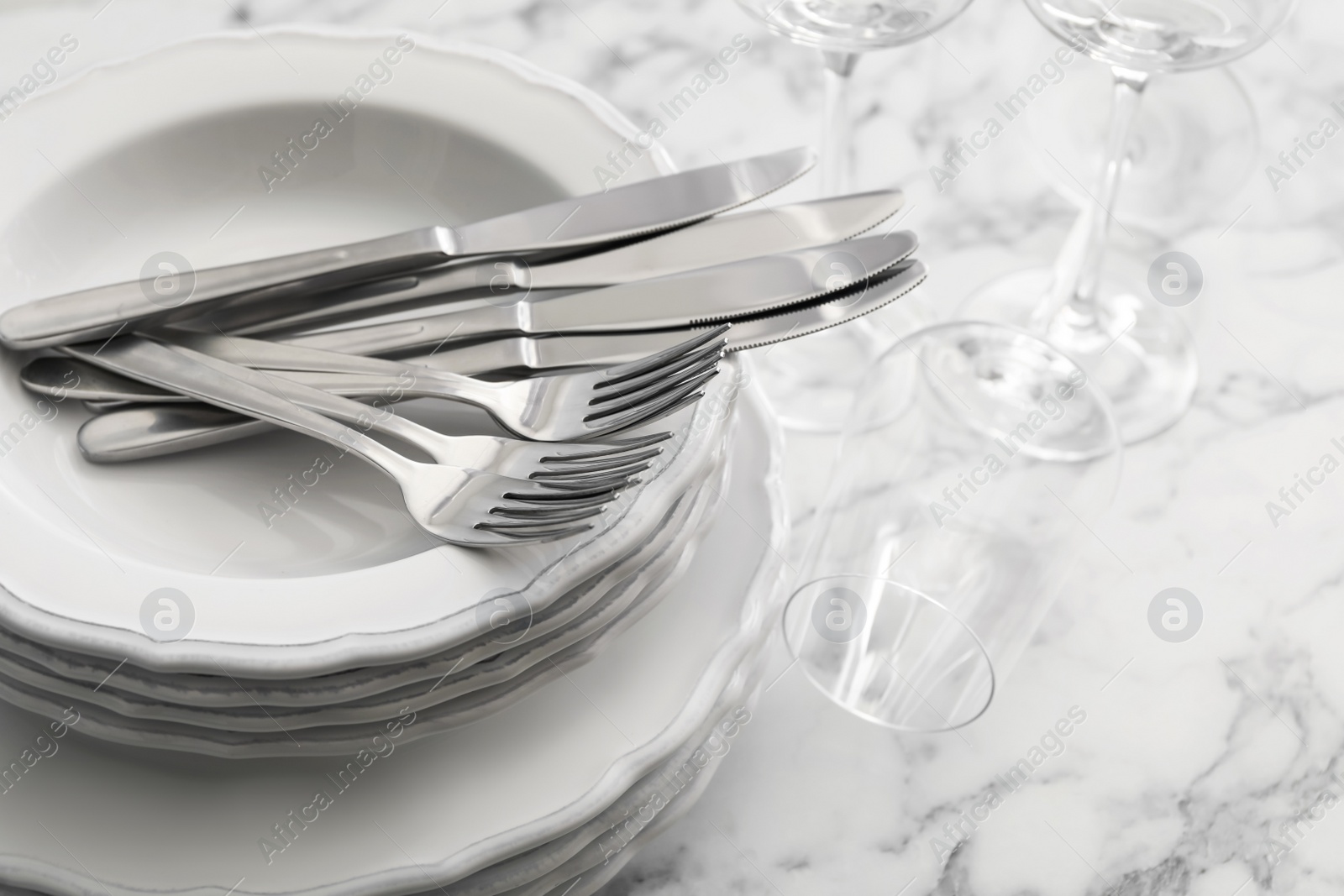 Photo of Plates, cutlery and glasses on white marble table, closeup