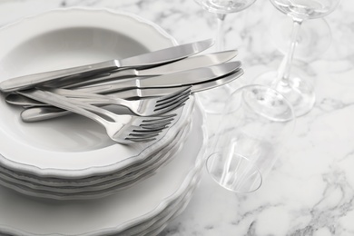 Plates, cutlery and glasses on white marble table, closeup