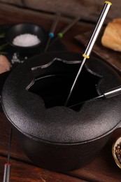 Fondue pot with forks on wooden table, closeup