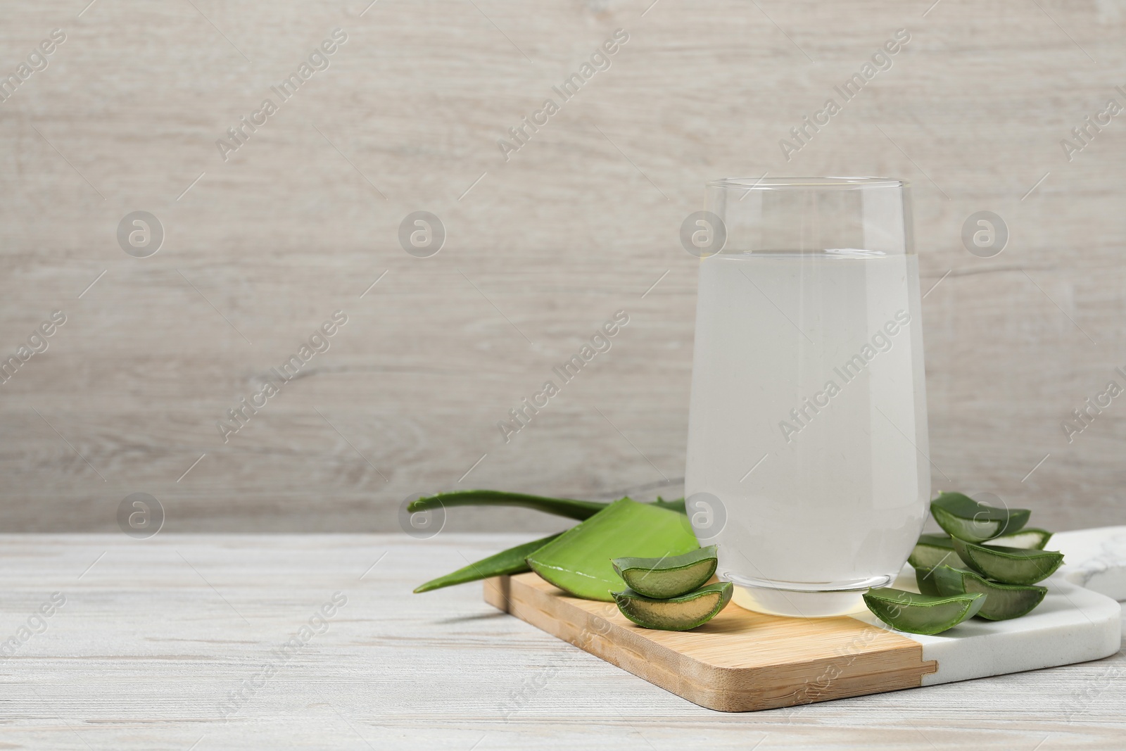 Photo of Tasty aloe juice in glass and cut fresh leaves on light wooden table, space for text