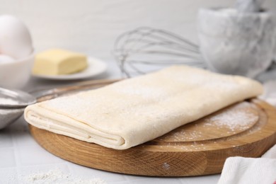 Photo of Raw puff pastry dough on white tiled table, closeup