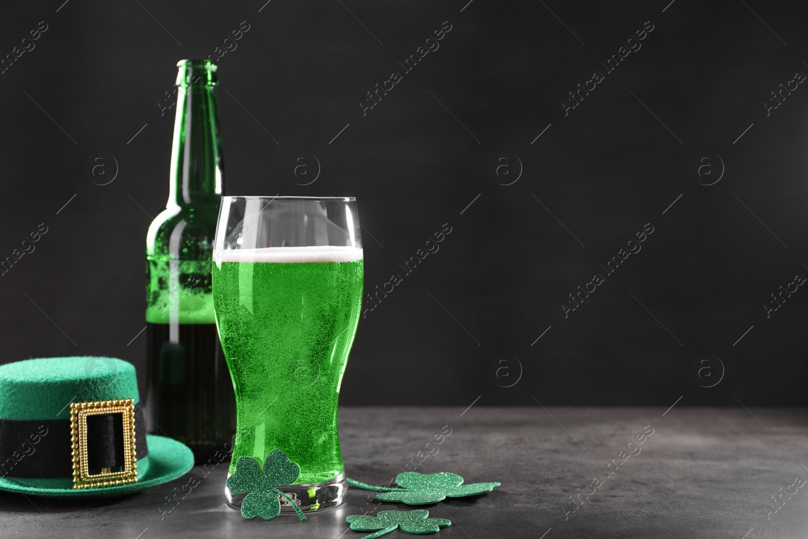 Photo of St. Patrick's day celebration. Green beer, leprechaun hat and decorative clover leaves on grey table. Space for text