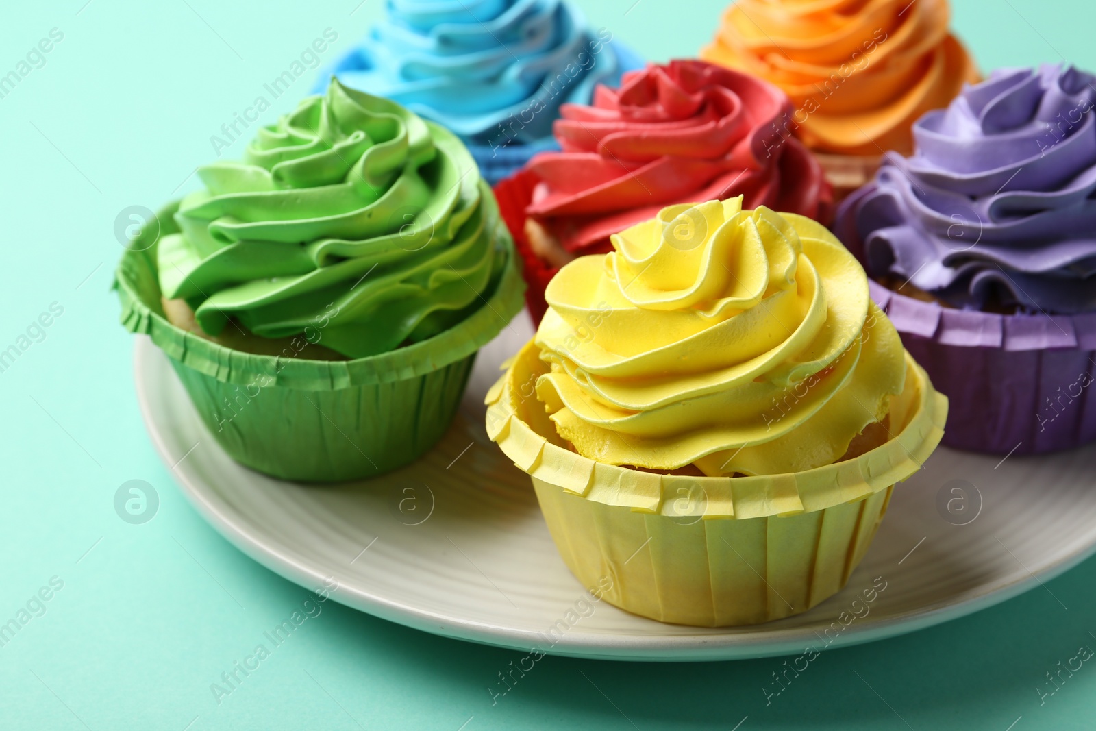 Photo of Plate with delicious bright cupcakes on turquoise background, closeup