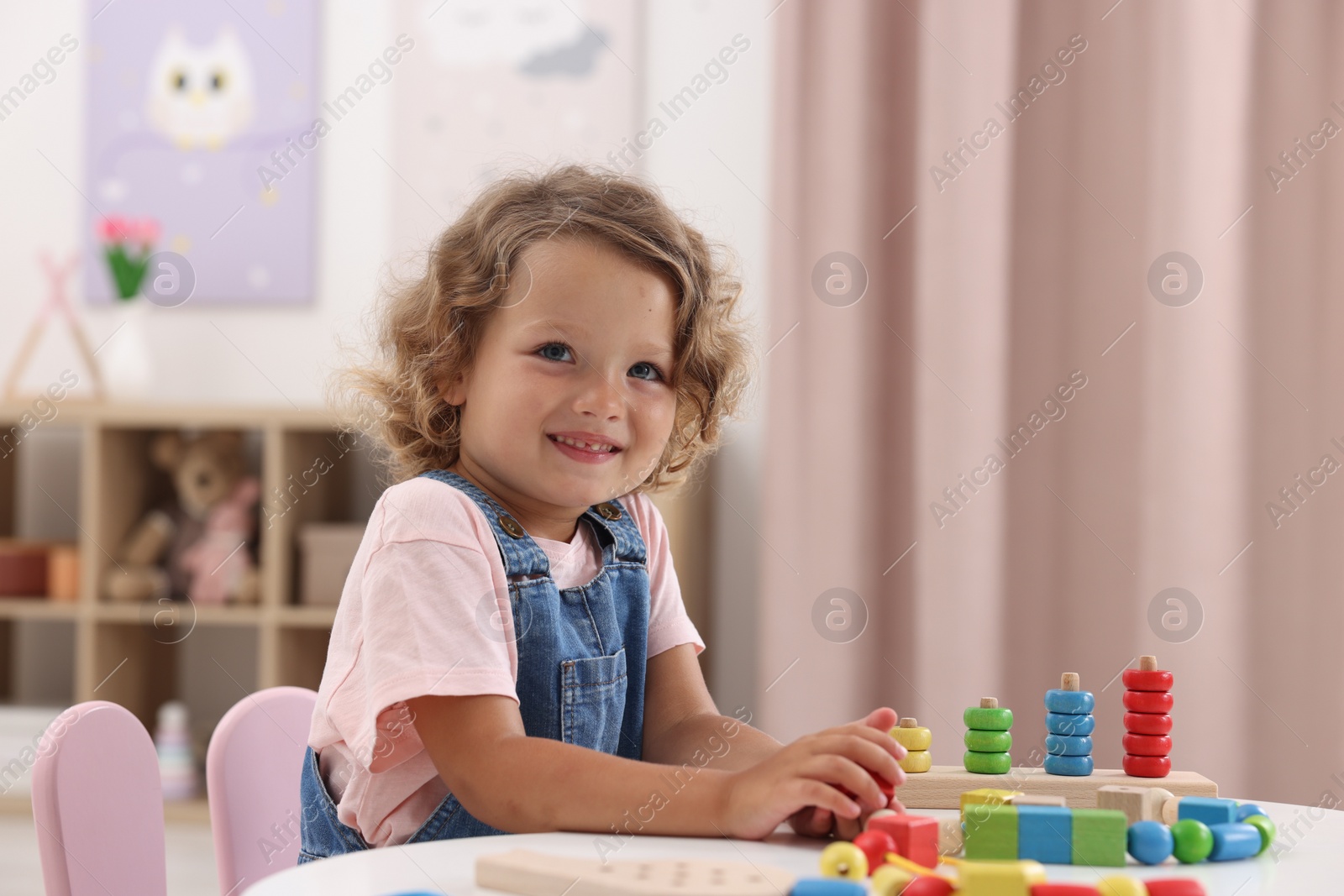 Photo of Motor skills development. Little girl playing with toys at table indoors