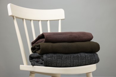 Photo of Stack of different warm sweaters on white chair against grey background