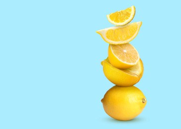 Stacked cut and whole lemons on pale light blue background, space for text