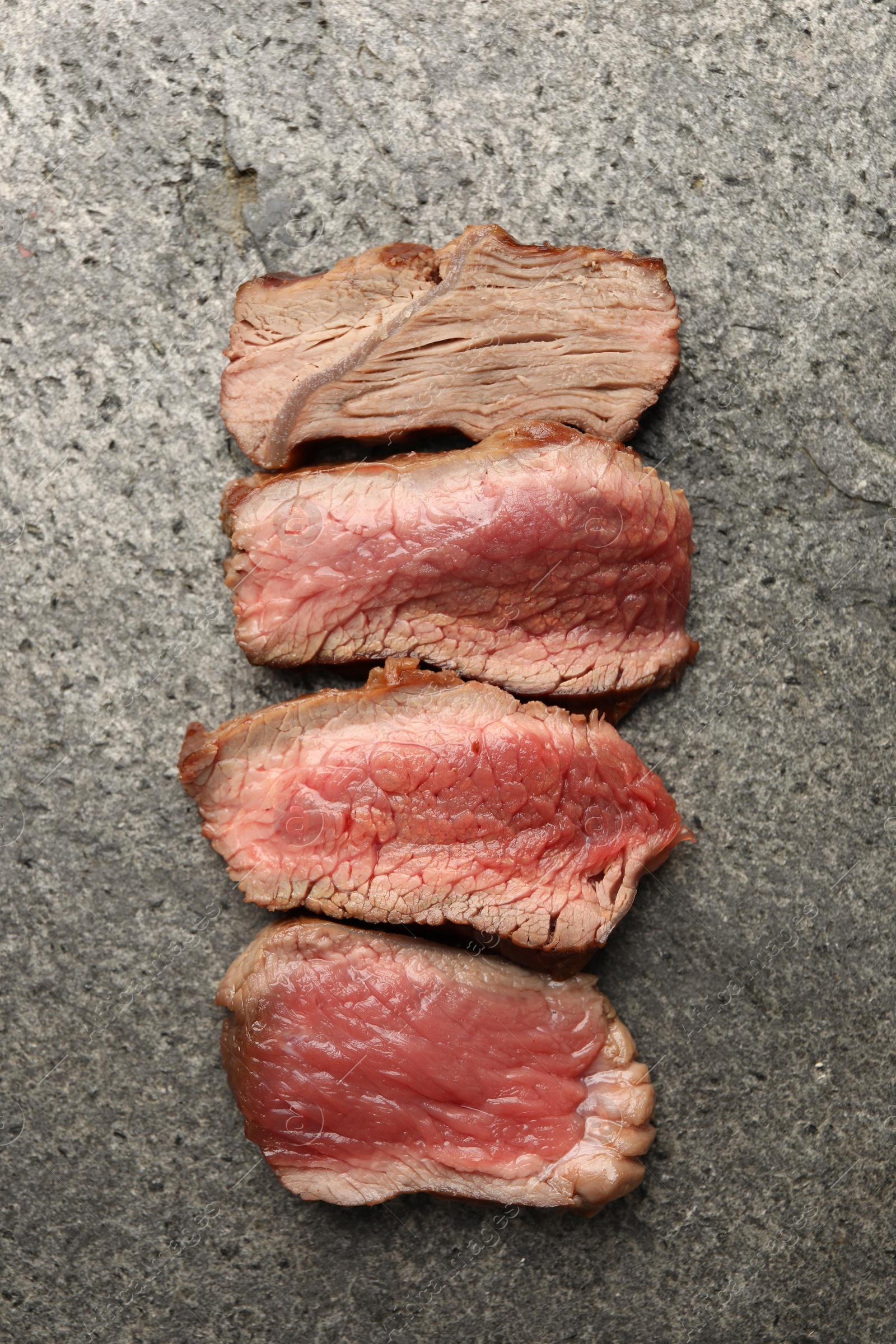 Photo of Delicious sliced beef tenderloin with different degrees of doneness on grey table, top view