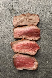 Photo of Delicious sliced beef tenderloin with different degrees of doneness on grey table, top view