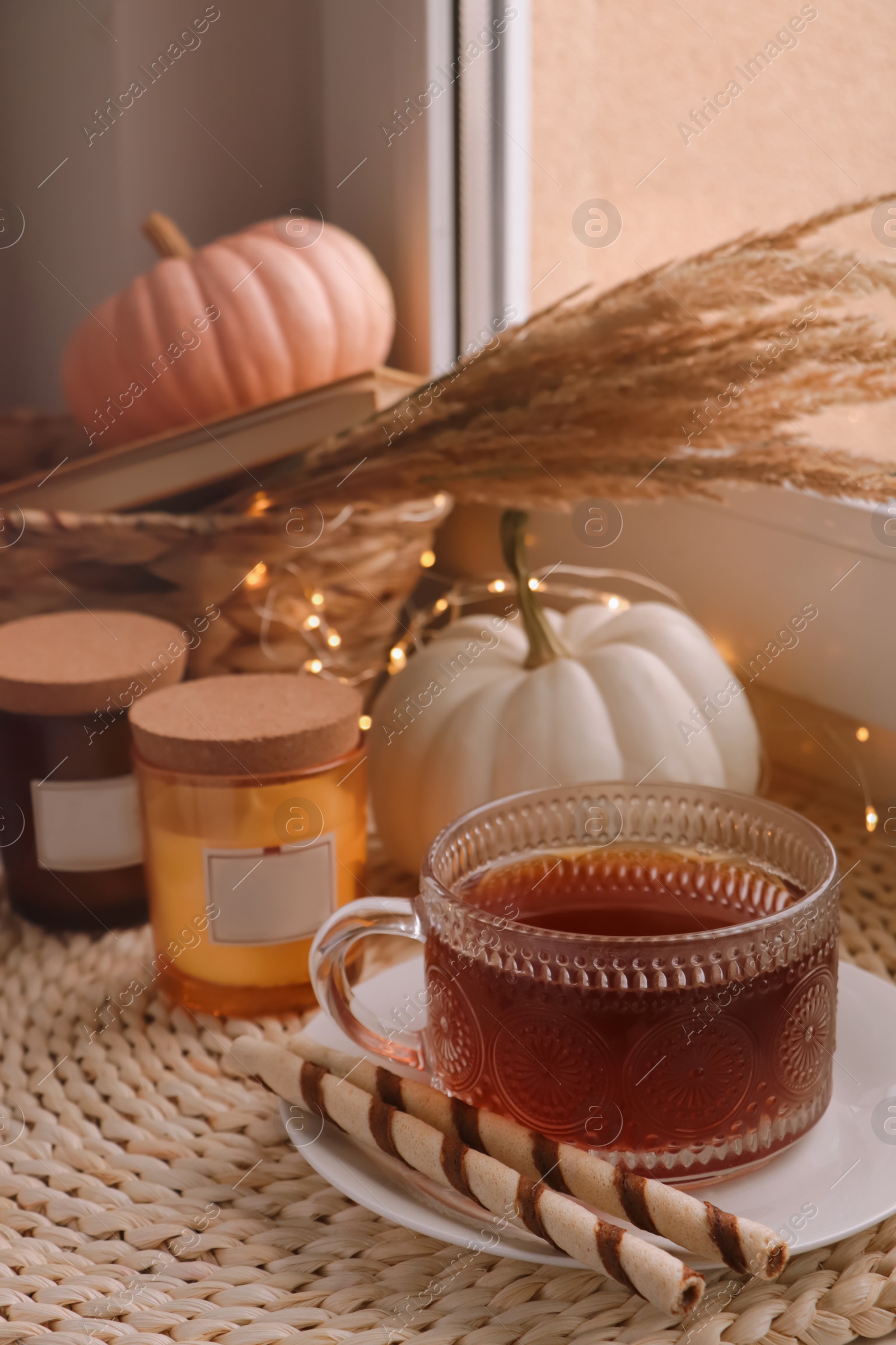 Photo of Cup of hot drink, cookies, candles and pumpkins on window sill indoors