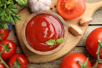 Tasty ketchup, fresh tomatoes, parsley and spices on wooden table, flat lay