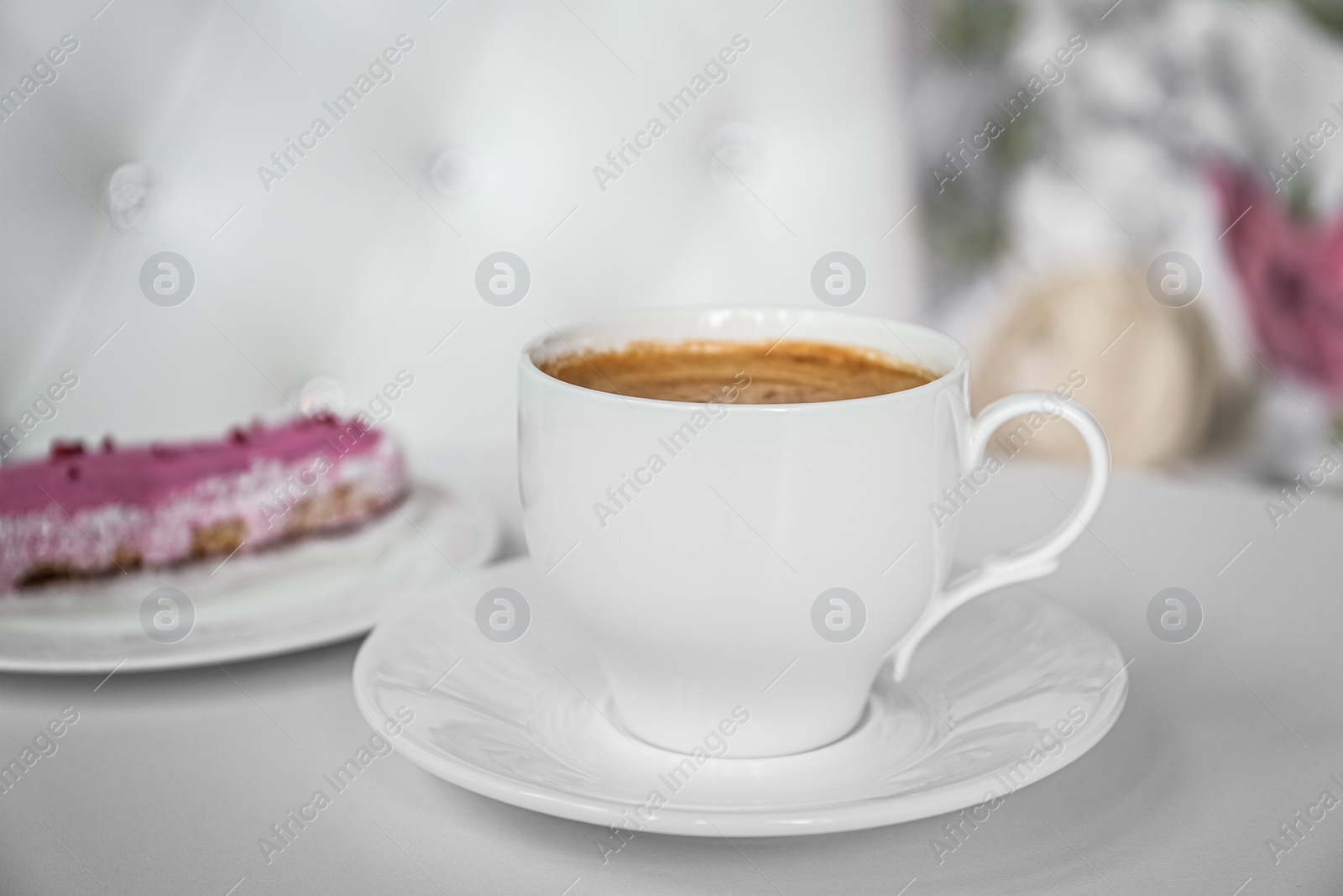 Photo of Cup of delicious aromatic coffee and eclair on white table indoors, closeup