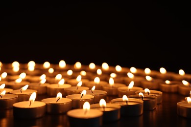 Burning candles on dark surface against black background