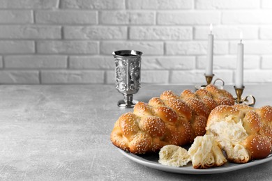 Photo of Homemade braided bread with sesame seeds and goblet on grey table, space for text. Traditional Shabbat challah