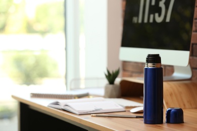 Photo of Modern thermos on wooden desk at workplace. Space for text
