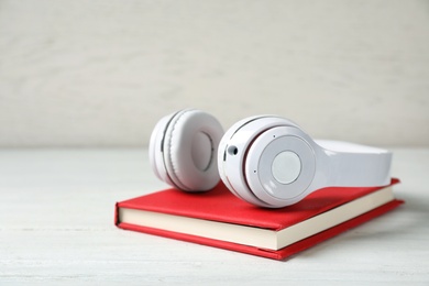 Photo of Modern headphones with hardcover book on wooden table