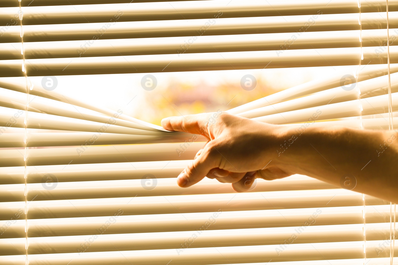 Photo of Man separating slats of white blinds indoors, closeup