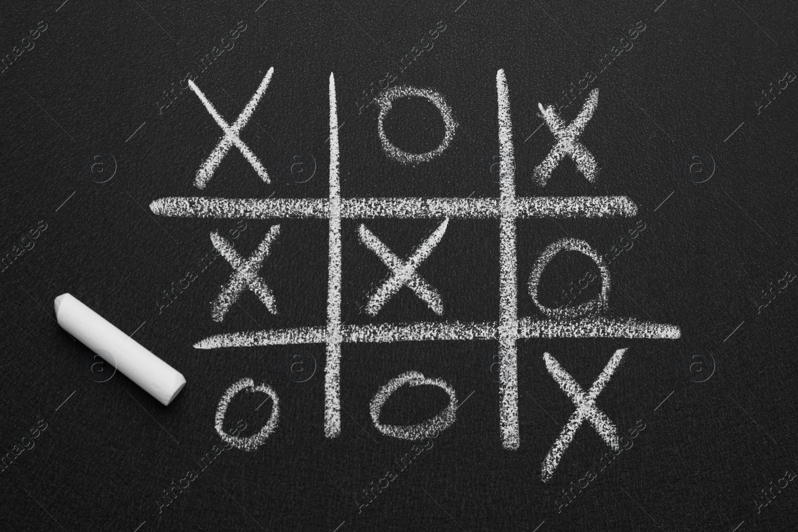 Photo of Tic tac toe game and piece of chalk on blackboard, top view