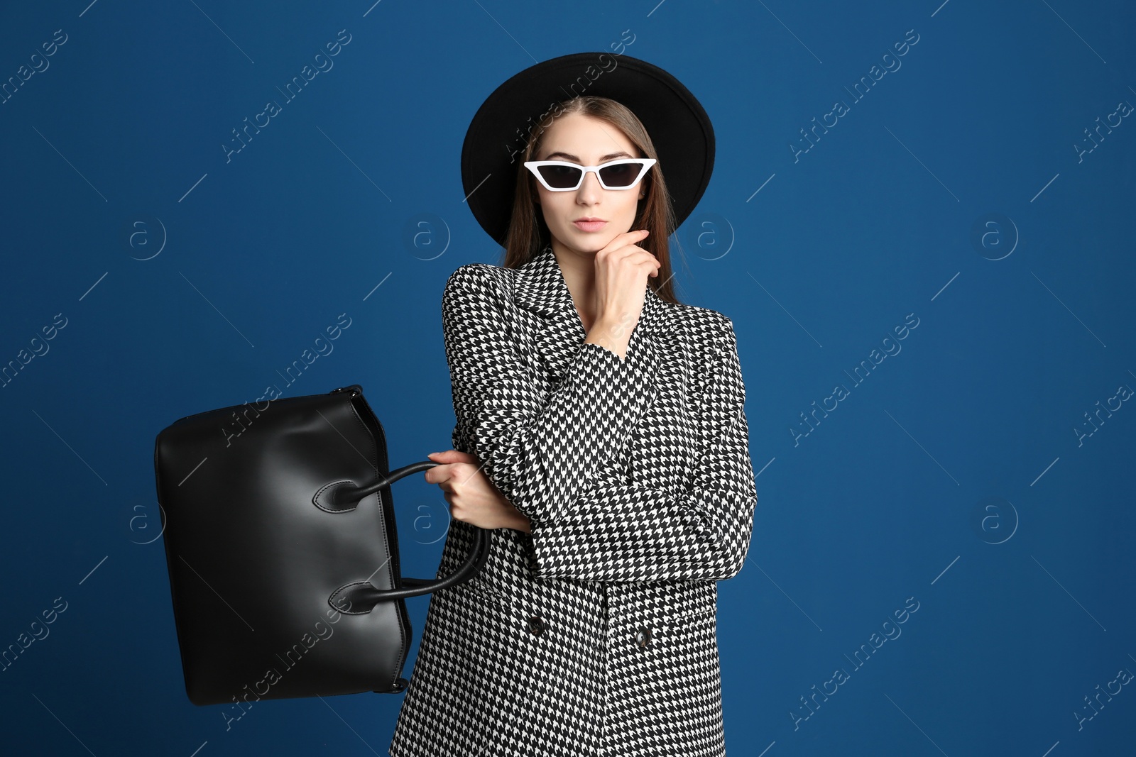 Photo of Beautiful young woman in sunglasses with stylish bag on blue background