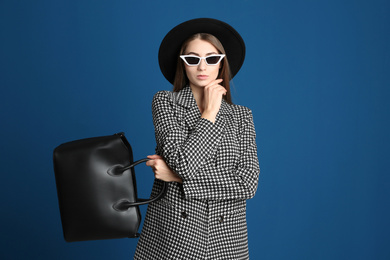 Beautiful young woman in sunglasses with stylish bag on blue background