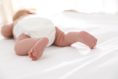 Photo of Cute little baby in diaper on bed at home, closeup