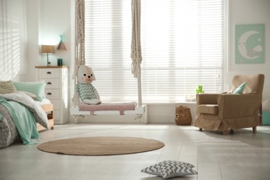 Photo of Stylish swing with toy in child's room. Interior design