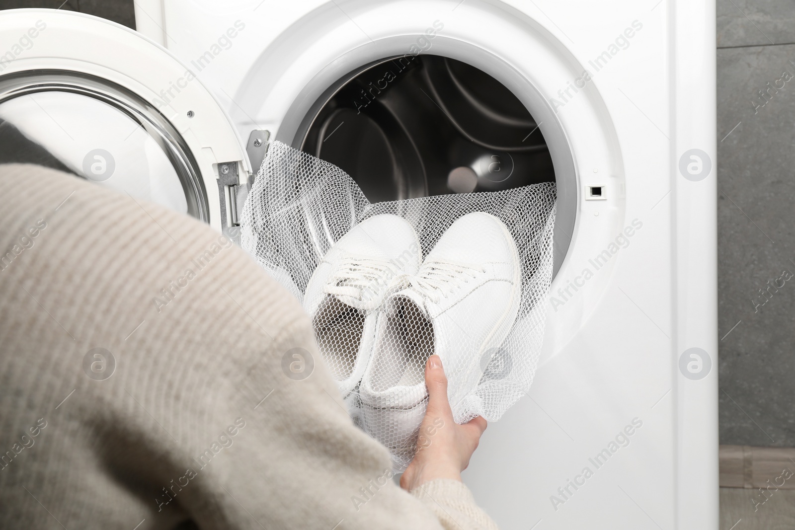 Photo of Woman putting stylish sneakers into washing machine, closeup