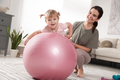 Photo of Mother doing exercise with her daughter on fitball at home