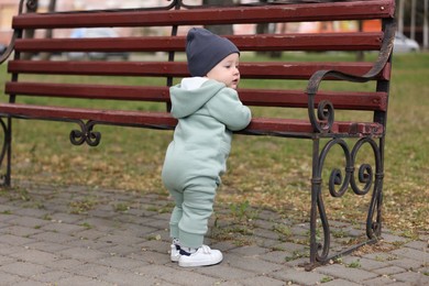 Photo of Little baby learning to walk near bench in park