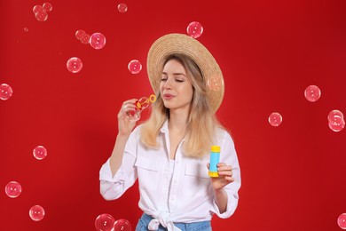 Young woman blowing soap bubbles on red background