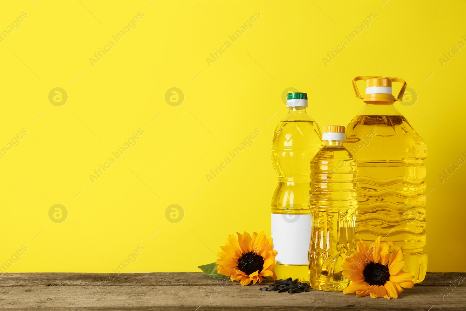Photo of Bottles of cooking oil, sunflowers and seeds on wooden table, space for text