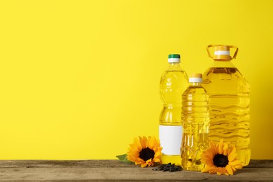Bottles of cooking oil, sunflowers and seeds on wooden table, space for text