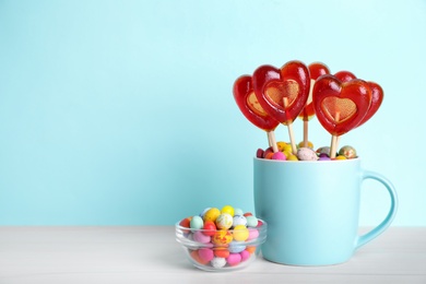 Delicious heart shaped lollipops and dragees on table against light blue background. Space for text