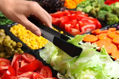 Photo of Young woman taking iceberg lettuce from salad bar, closeup