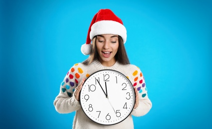 Photo of Woman in Santa hat with clock on light blue background. Christmas countdown